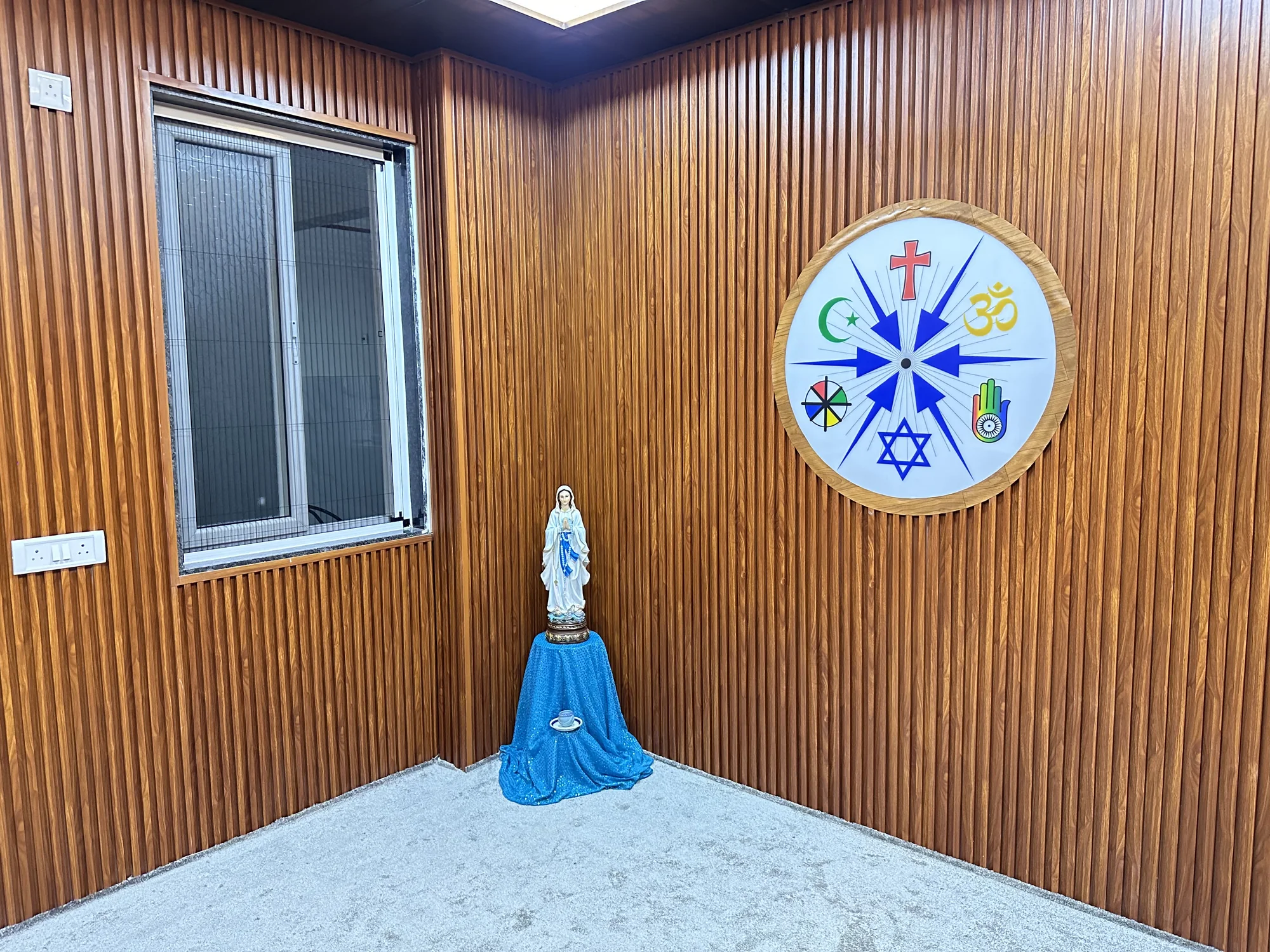 Prayer and reflection space with Mother Mary statue and multi-faith emblem